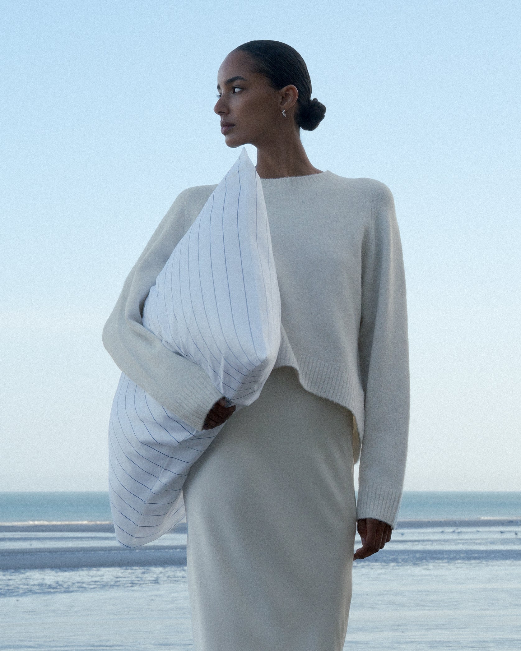 Model wearing light sweater and light skirt holding a striped pillow case from Abate